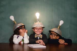 young kids with homemade thinking caps, one in middle has light bulb lit up