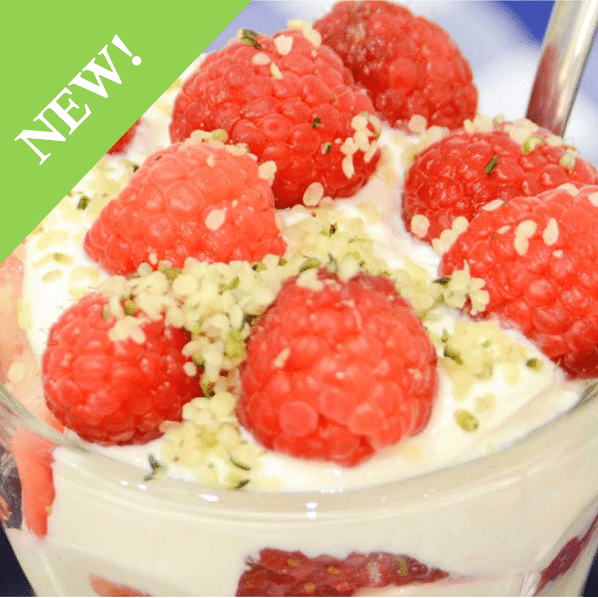 close up of parfait in glass cup tops with large raspberries and granola flakes