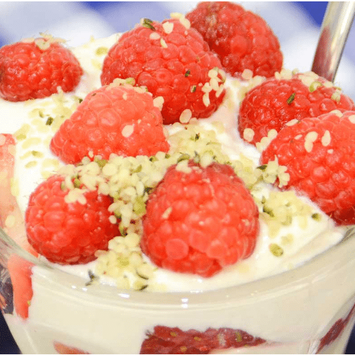 close up of parfait in glass cup tops with large raspberries and granola flakes