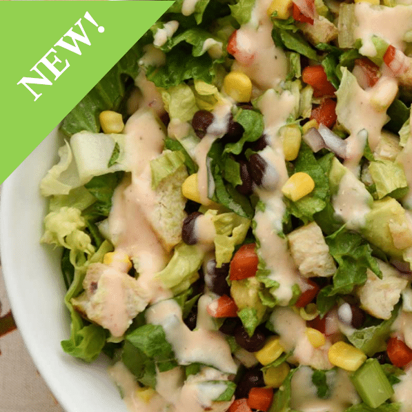 close up of chopped salad with corn, black beans, tomatoes, onion and drizzles of creamy dressing