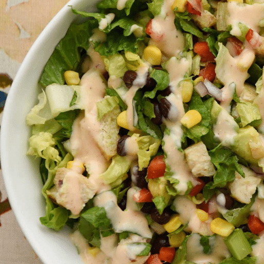 close up of chopped salad with corn, black beans, tomatoes, onion and drizzles of creamy dressing
