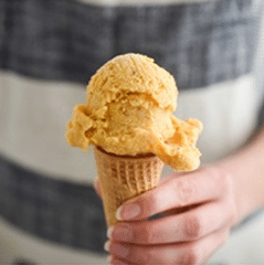 cream colored ice cream in cone held by person in striped dress