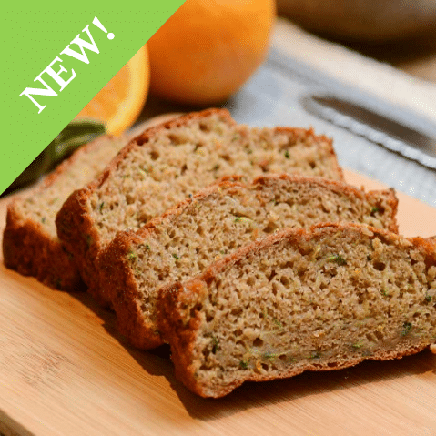 sliced zucchini bread layered on cutting board next to oranges and zucchini