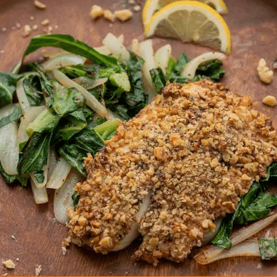 walnut-crusted tilapia with greens and lemon on wood plate
